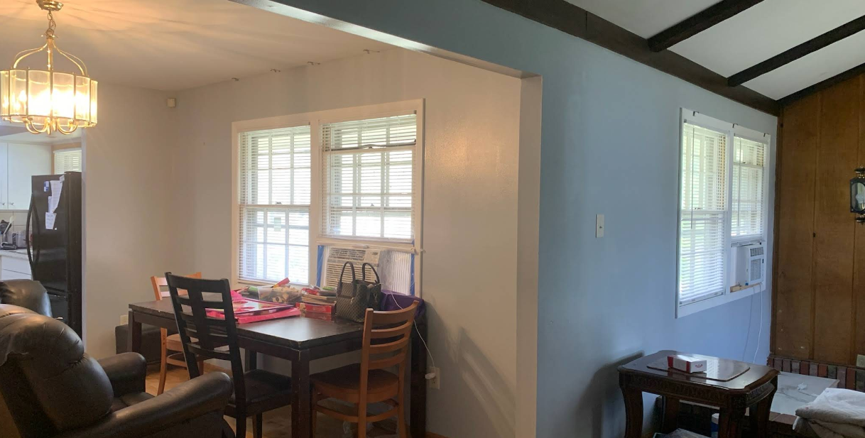 Interior of a home with dining area, windows, and living area with wood ceiling beams.