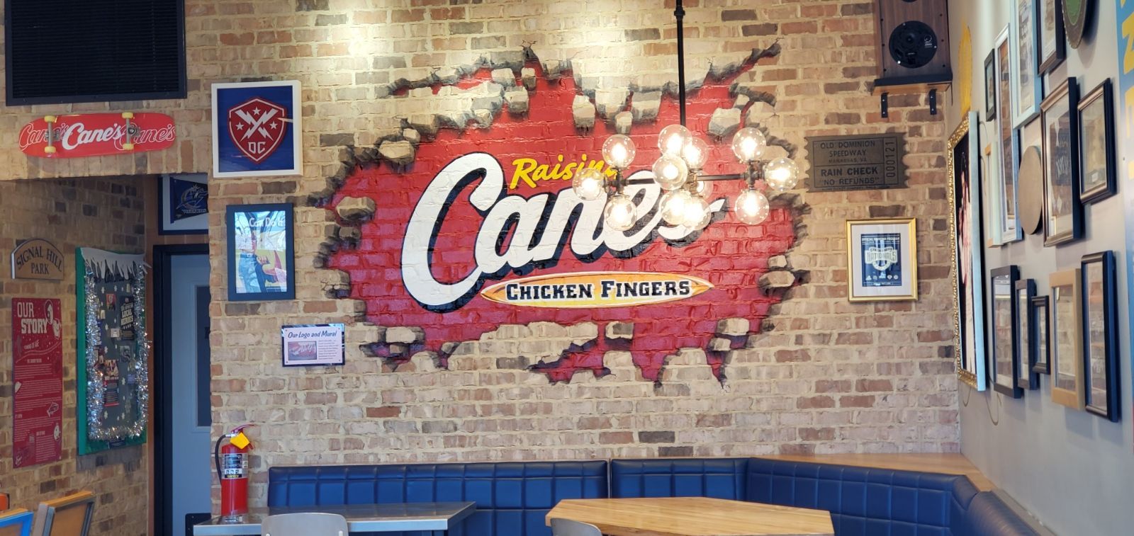 Interior of a Raising Cane's restaurant, featuring a brick wall with the restaurant's logo and framed memorabilia.