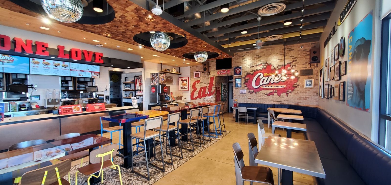 The interior of a modern Cane's restaurant, featuring dining tables, bar-style seating, and branded wall decor.