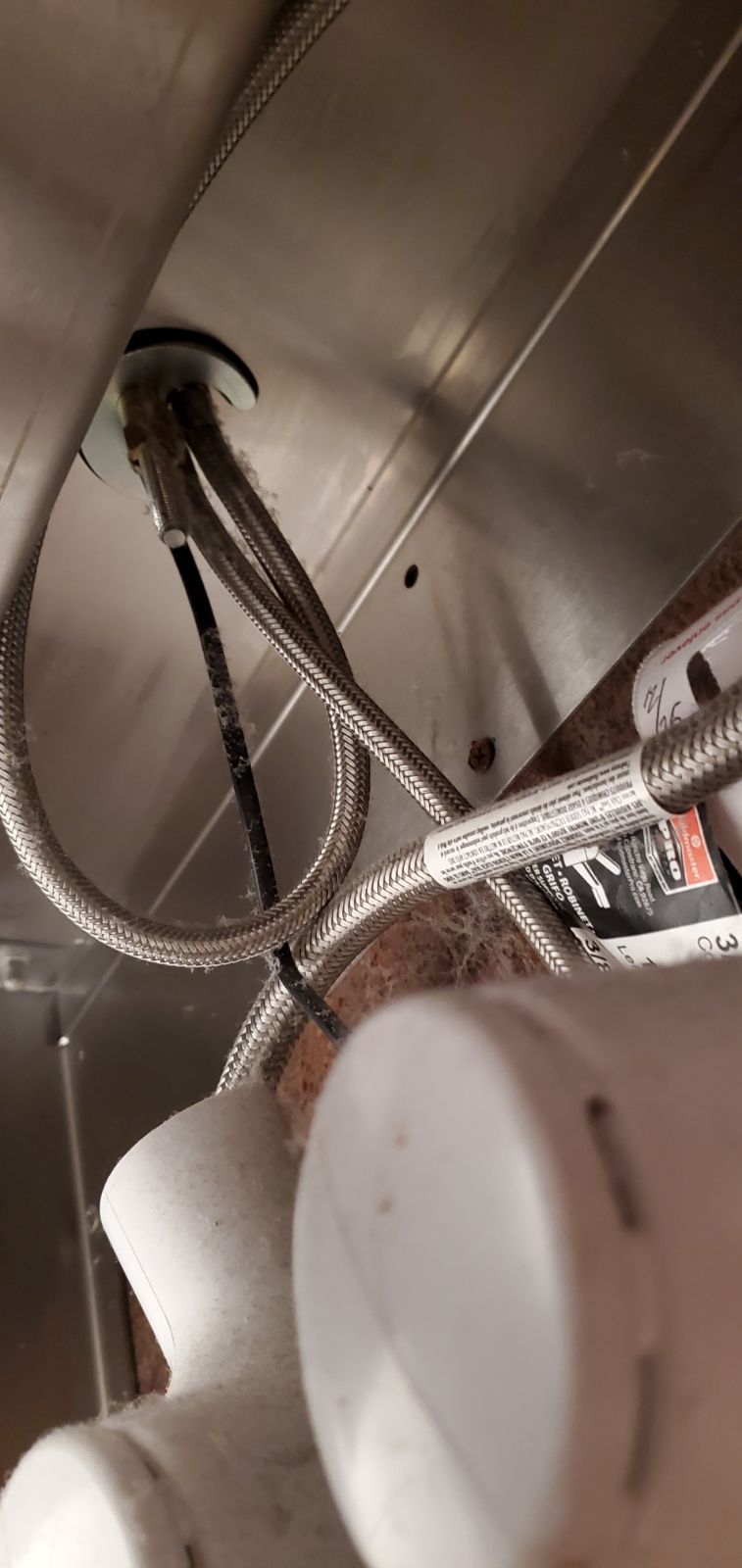A low-angle view of stainless steel braided hoses and plumbing pipes connected beneath a metal sink.