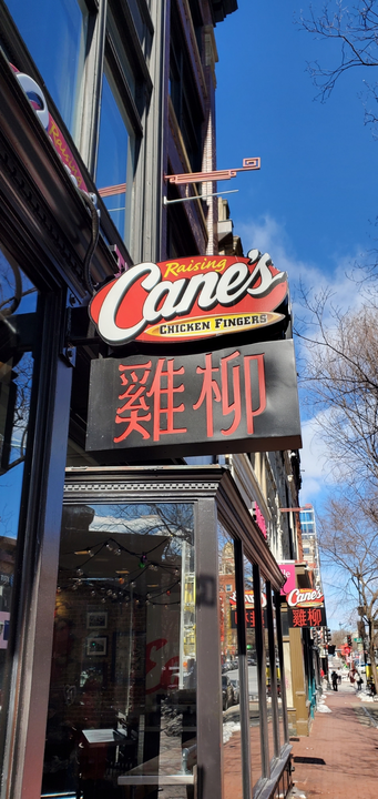 A vertical view of a Raising Cane's storefront sign with Chinese characters for 