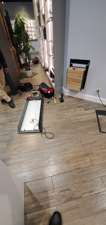 A person works on a floor installation project with tools and a detached light fixture in a modern interior space.