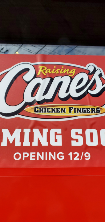 A red sign for Raising Cane's Chicken Fingers announcing it is coming soon and will be opening on 12/9.