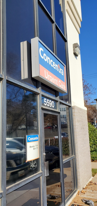 A street-level view of a Concentra urgent care center entrance with a sign and the address 5590 on a glass door.