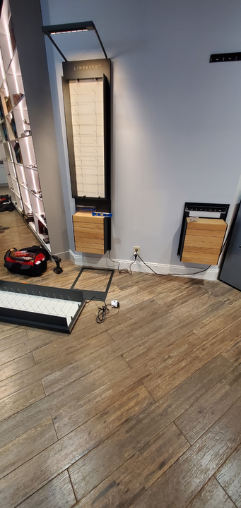 A partially installed display system with wooden cabinets and illuminated shelves against a gray wall in a room under repair.
