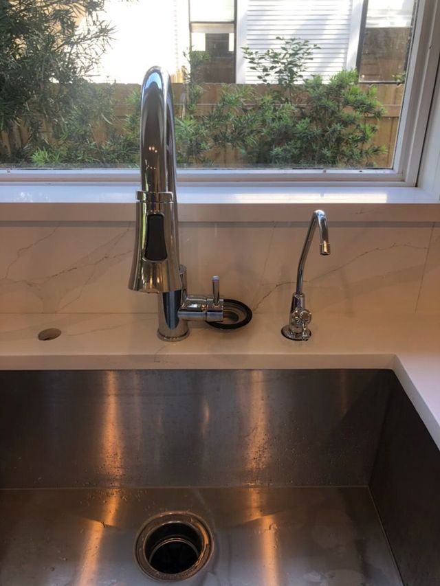 Stainless steel kitchen sink with faucet, reverse osmosis faucet, and window overlooking greenery.