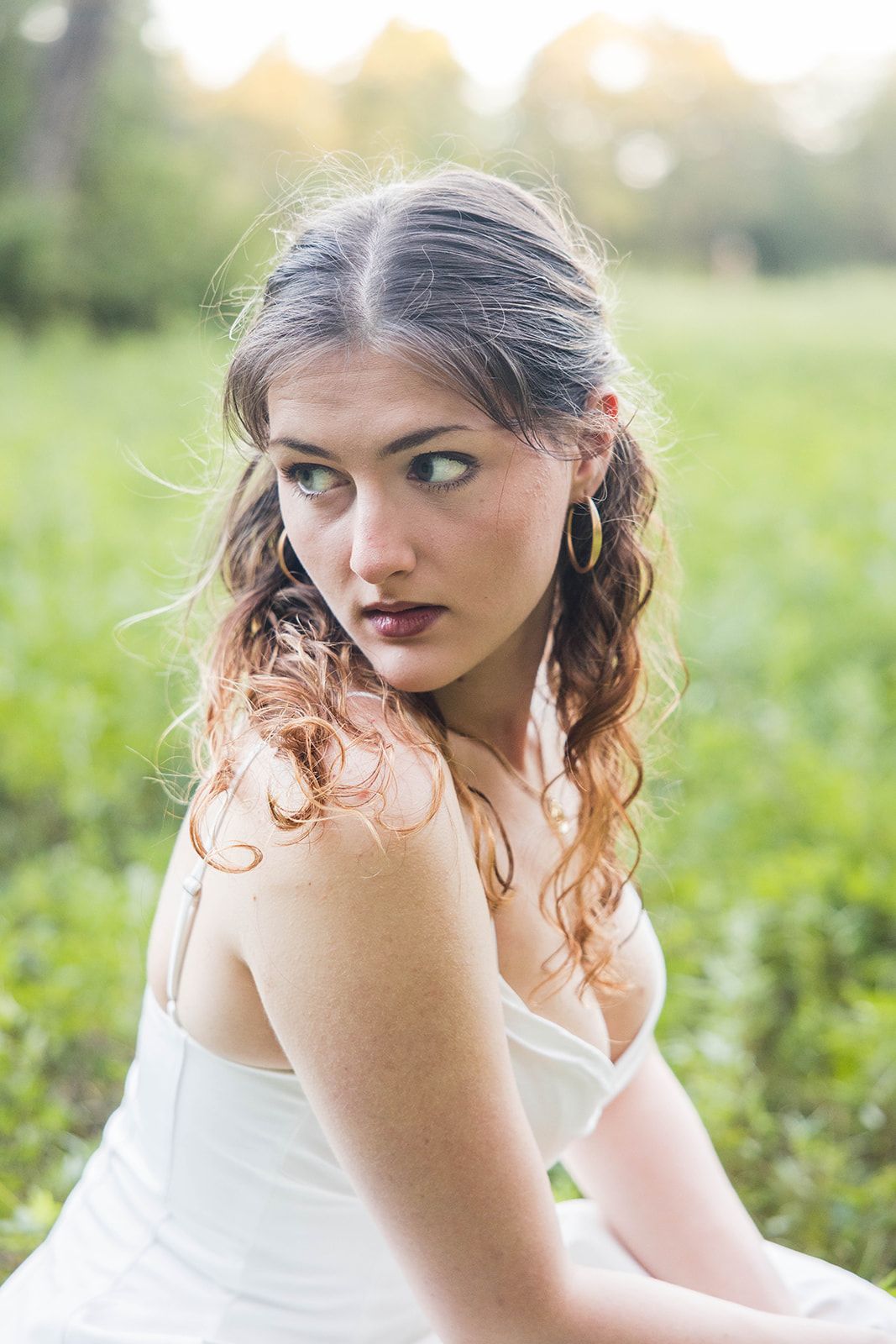 A person with long brown hair, wearing a white tank top and a red jacket, poses against a plain gray background.