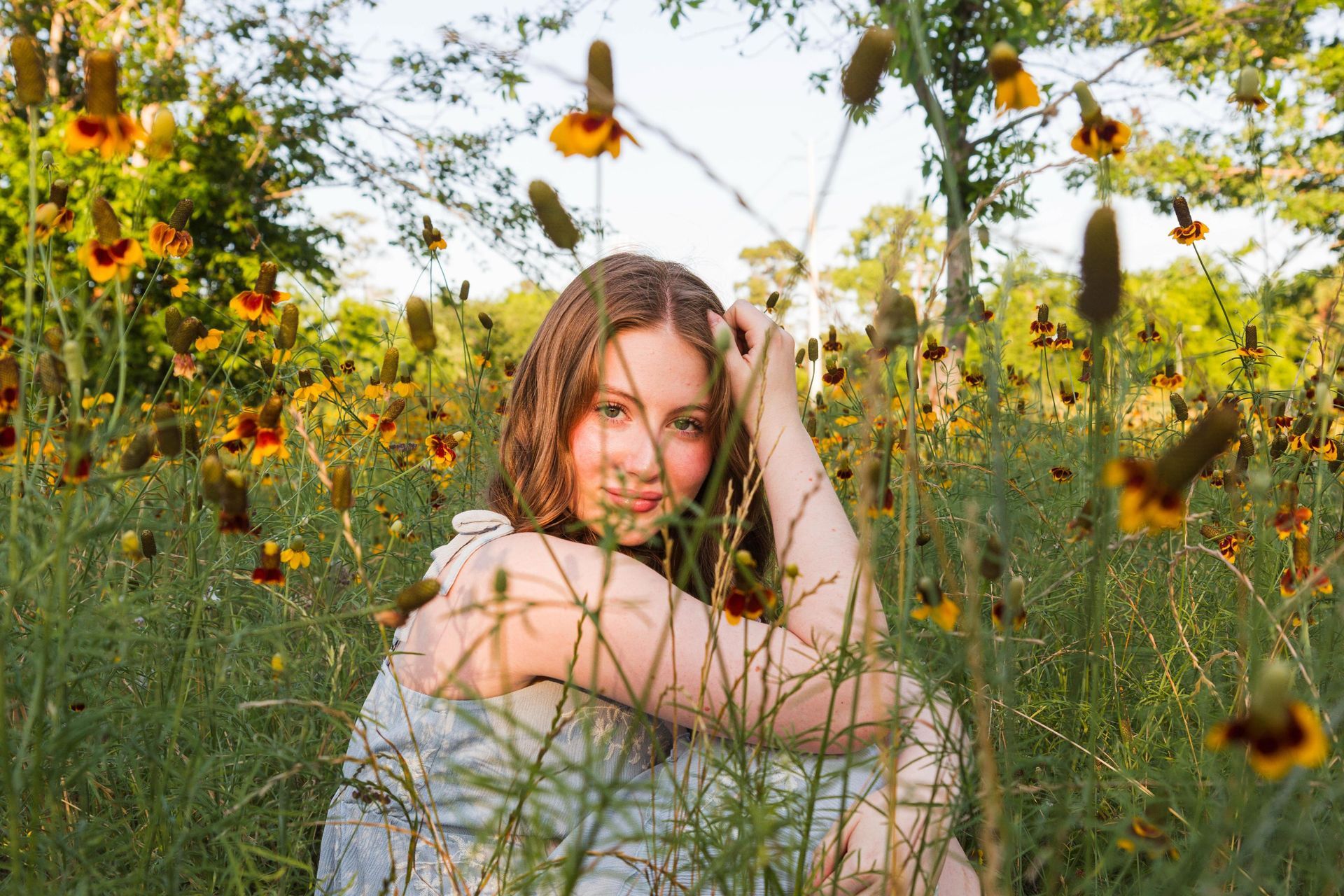 A person with dark hair wearing a white top lying in a field of bluebonnet flowers and looking upward.