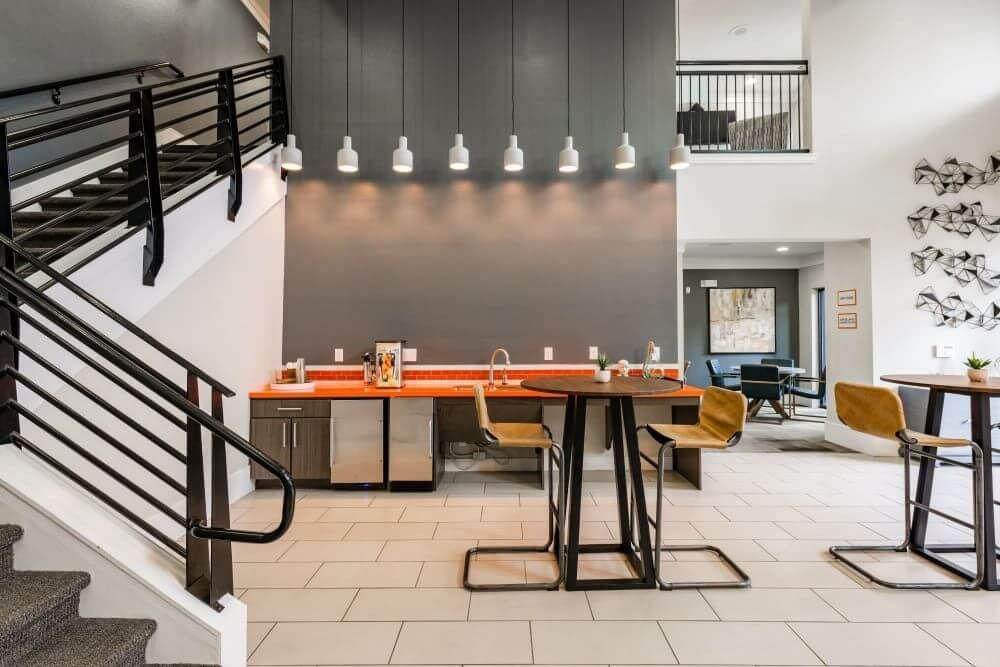 Interior common area with stairs, a bar with stools, and overhead lighting against a gray wall at Marquis Seven Meadows, offering apartments in Katy ISD.