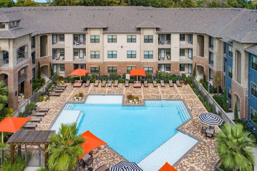 Aerial view of a heart-shaped pool surrounded by lounge chairs, orange umbrellas, and an apartment complex at Marquis Seven Meadows.