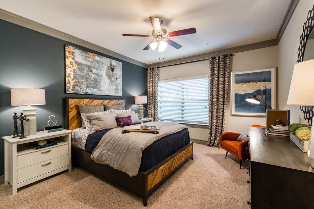 Bedroom with blue accent wall, bed with wooden headboard, orange chair, and large abstract art at Marquis Seven Meadows, offering apartments in Katy, TX.