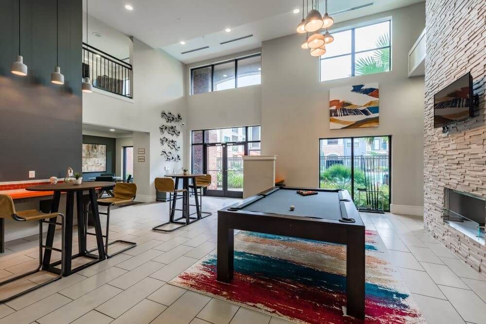 Spacious apartment lounge with a pool table, bar seating, large windows, and decorative artwork at Marquis Seven Meadows, offering apartments in Katy ISD.
