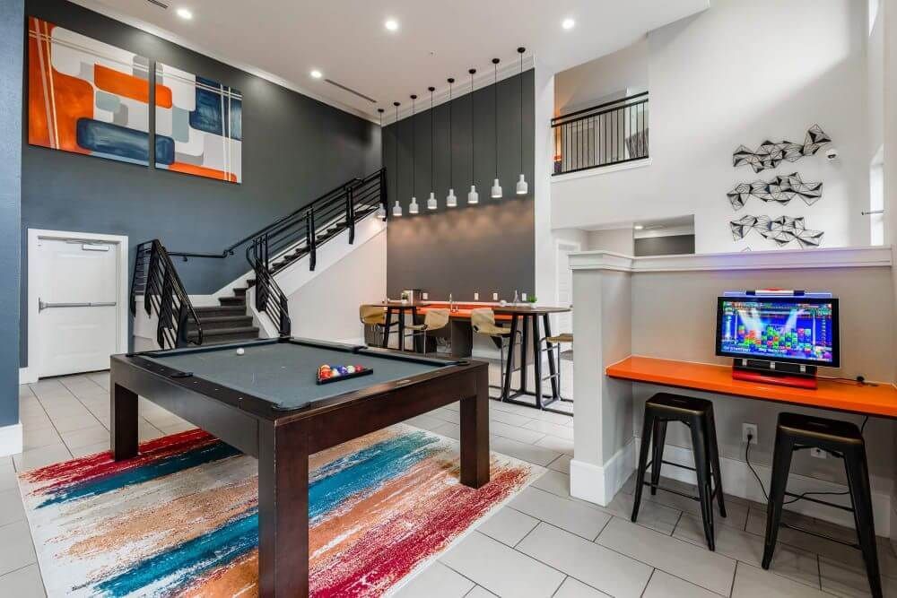 Game room with pool table, stairs, and a gaming console at Marquis Seven Meadows, offering apartments in Katy ISD. Orange, gray, and white decor.