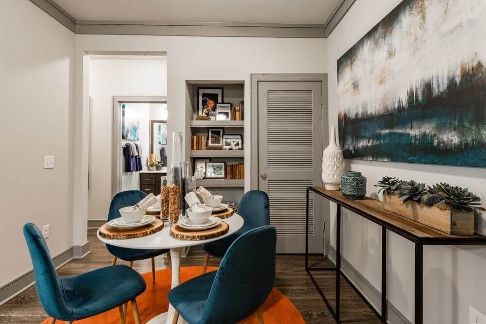 Dining area with white table, teal chairs, orange rug, and artwork at Marquis Seven Meadows, offering apartments in Katy, TX.