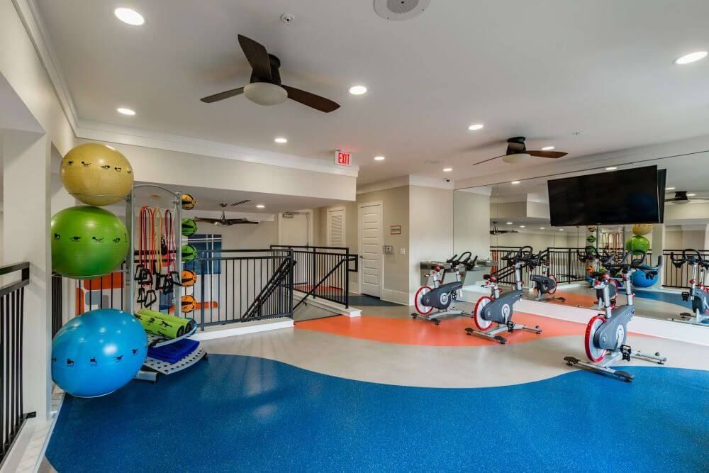 Gym with exercise bikes, fitness balls, and mirrors at Marquis Seven Meadows, offering apartments in Katy ISD. Blue, orange, and gray flooring.