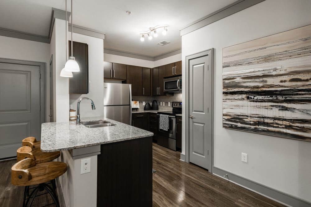 Kitchen with granite island, brown cabinets, stainless steel appliances, and wood flooring at Marquis Seven Meadows, offering apartments in Katy, TX.