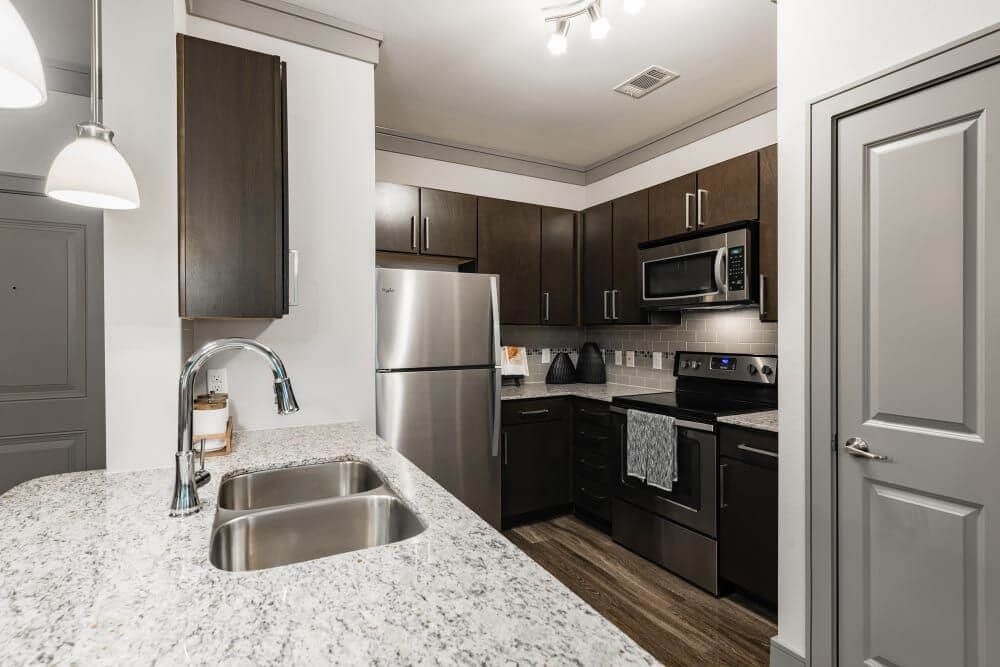 Kitchen with granite countertops, stainless steel appliances, and dark wood cabinets at Marquis Seven Meadows, offering apartments in Katy, TX.