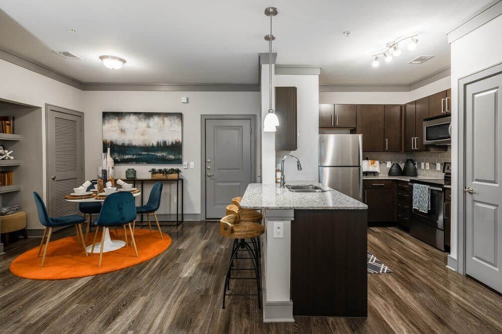 Modern kitchen and dining area with an island, dark cabinets, and wood flooring at Marquis Seven Meadows, offering apartments in Katy, TX. A table is set with blue chairs.