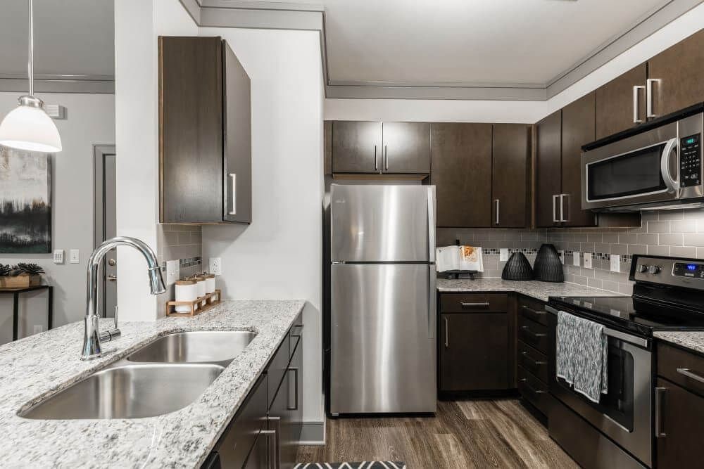Modern kitchen featuring stainless steel appliances, dark cabinets, and granite countertops at Marquis Seven Meadows, offering apartments in Katy, TX.