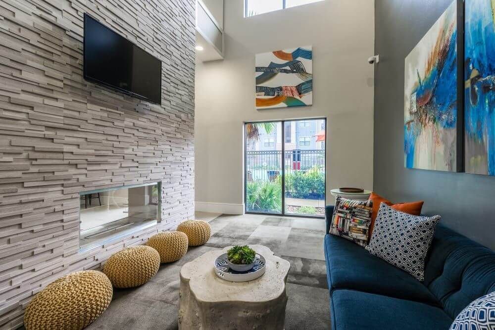 Clubhouse with stone fireplace, blue sofa, patterned pillows, art, and a stone coffee table at Marquis Seven Meadows, offering apartments in Katy ISD.