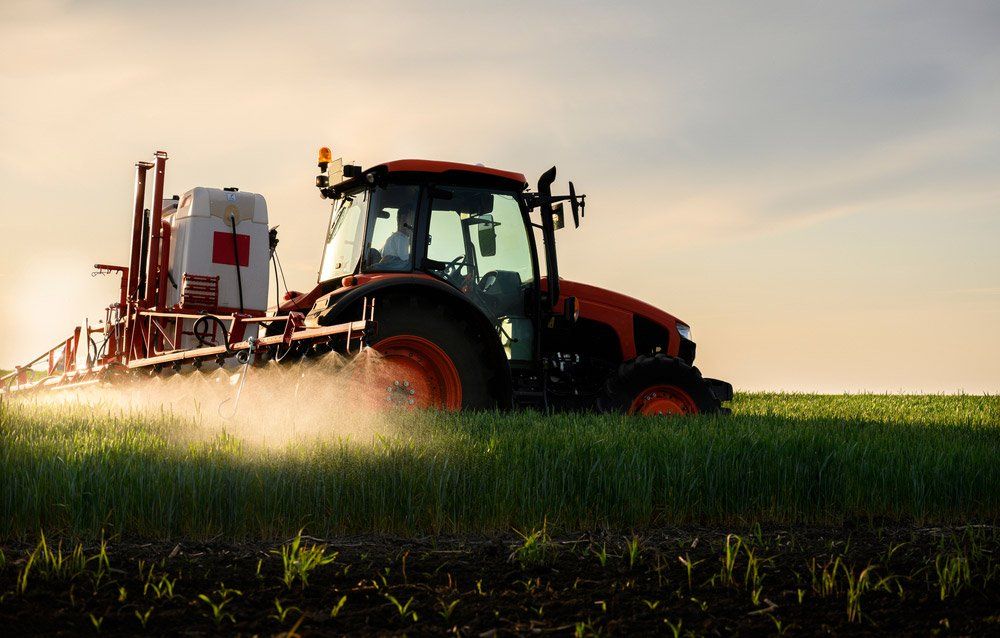 Tractor Spraying Pesticides Over A Green Field — Gloucester Rural Supplies in Gloucester, NSW