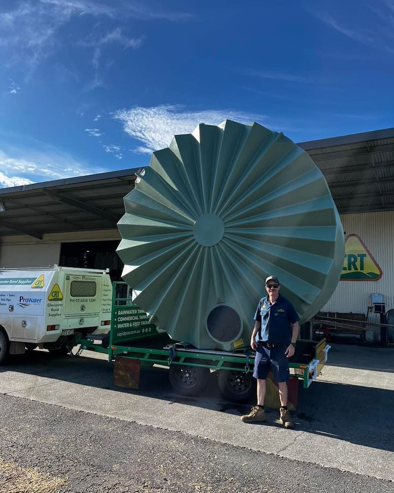 Man Stands by Large Green Water Tank on Trailer in Front of Building — Gloucester Rural Supplies in Bulahdelah, NSW