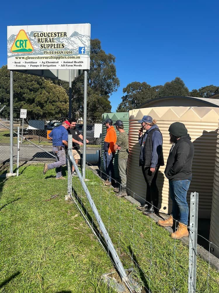 Group Near Water Tanks by Rural Supply Store Sign — Gloucester Rural Supplies in Bulahdelah, NSW