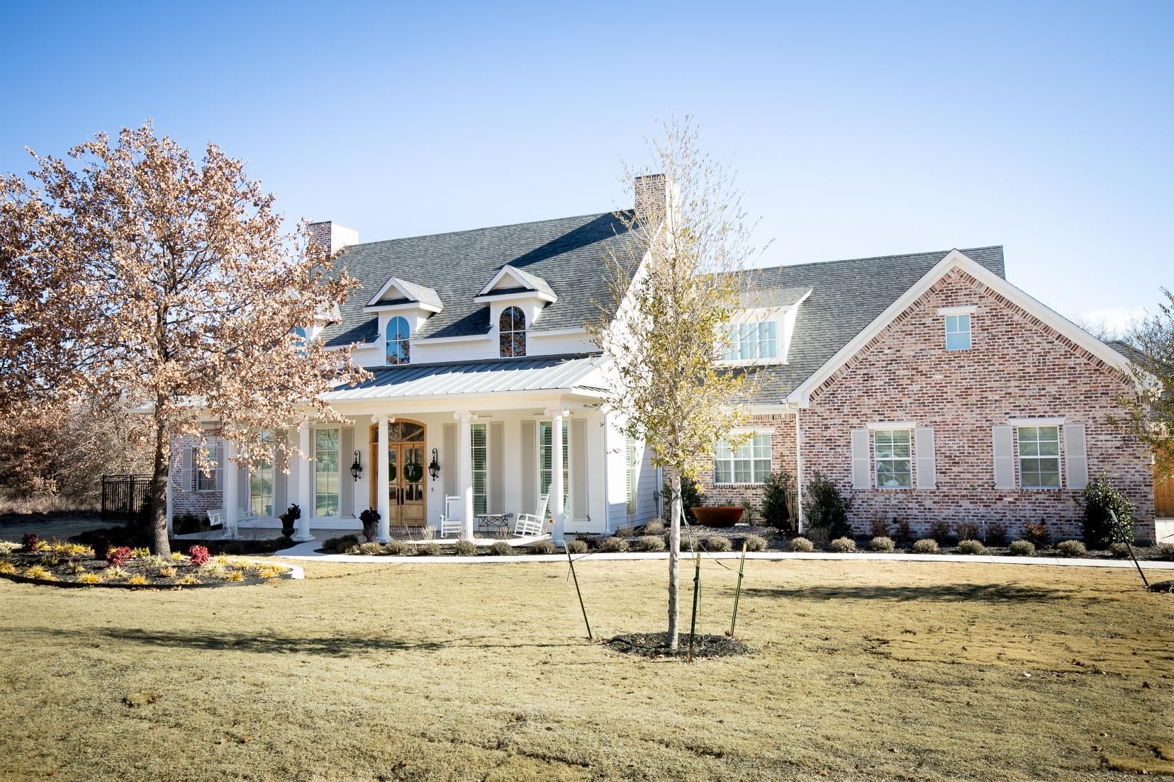 A large brick house with a large porch and trees in front of it.