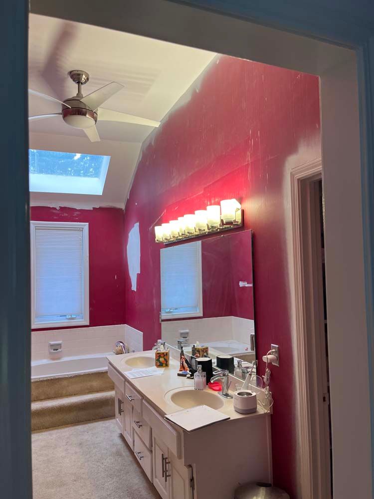 Bathroom with pink walls, white vanity, large mirror, and a skylight over the bathtub