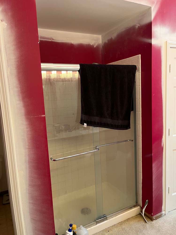 Bathroom with glass shower enclosure, red walls, and a dark towel hanging inside.