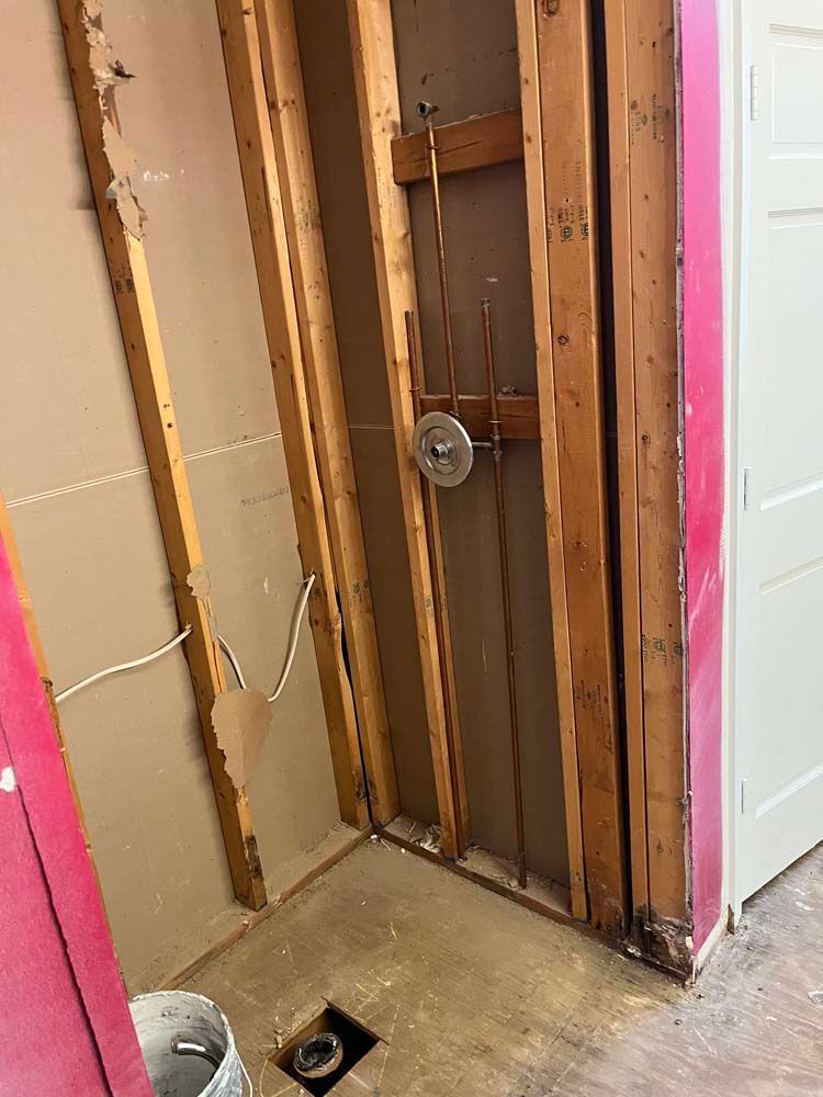 Bathroom wall opened to studs with exposed plumbing and wiring, showing a renovation in progress.