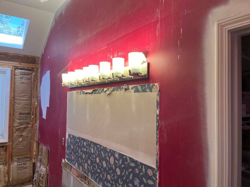 Hallway with red walls, wall sconce lights, and floral wallpaper trim above wood paneling.