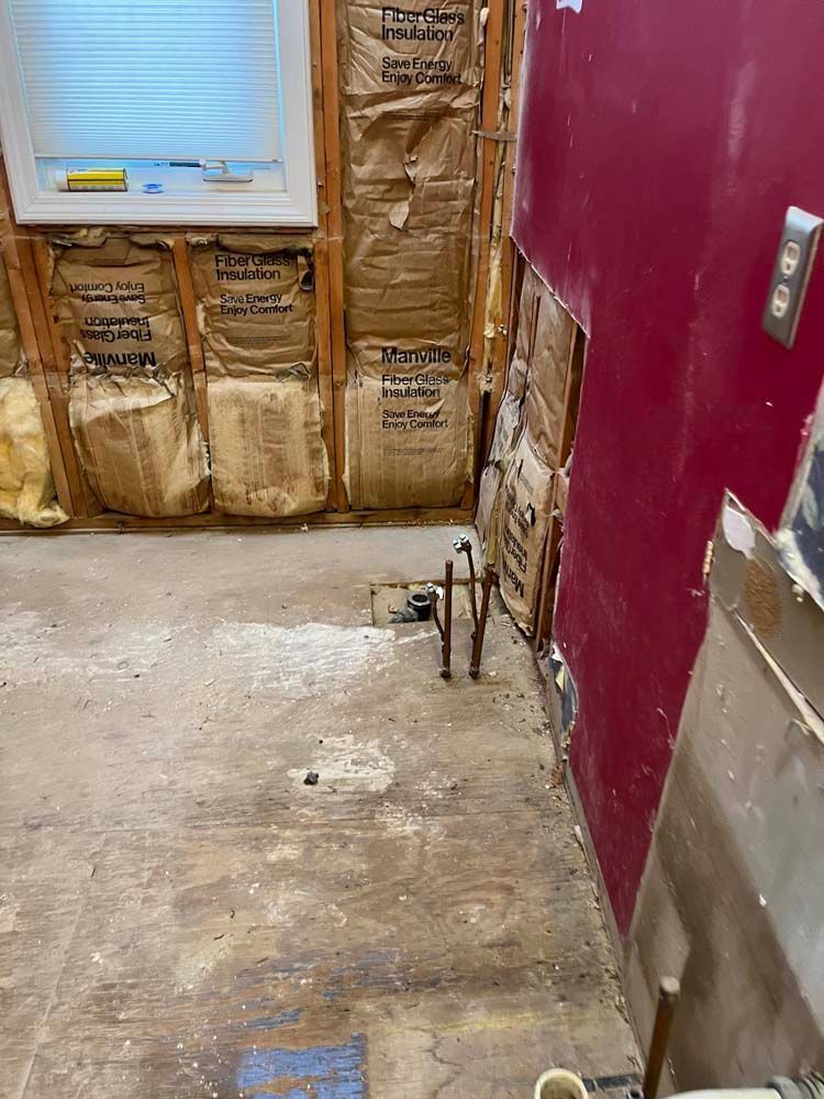 Unfinished room with exposed wall studs, torn insulation, and a maroon wall beside a concrete floor.