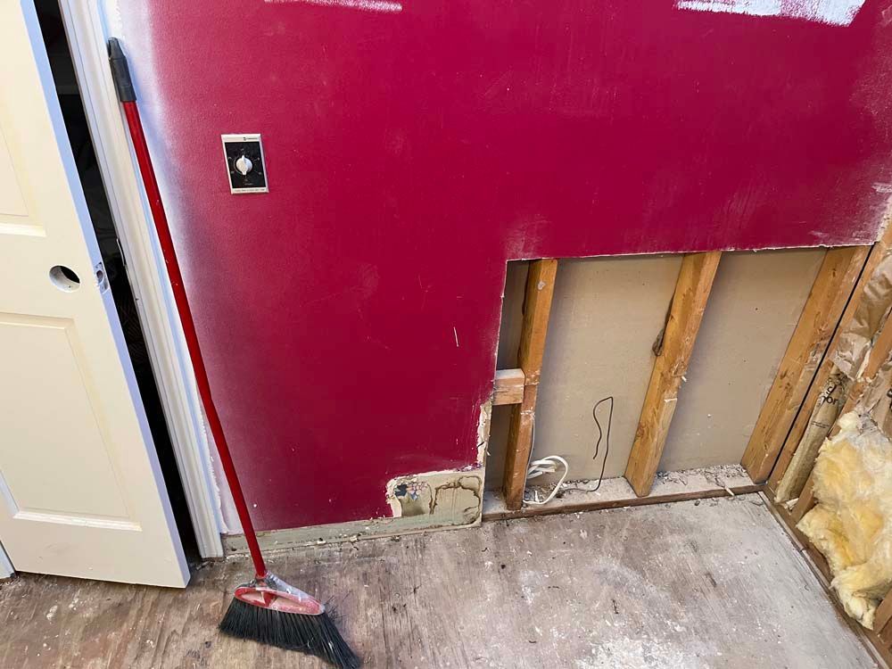 Partially demolished red wall with exposed studs and a broom in a room under renovation