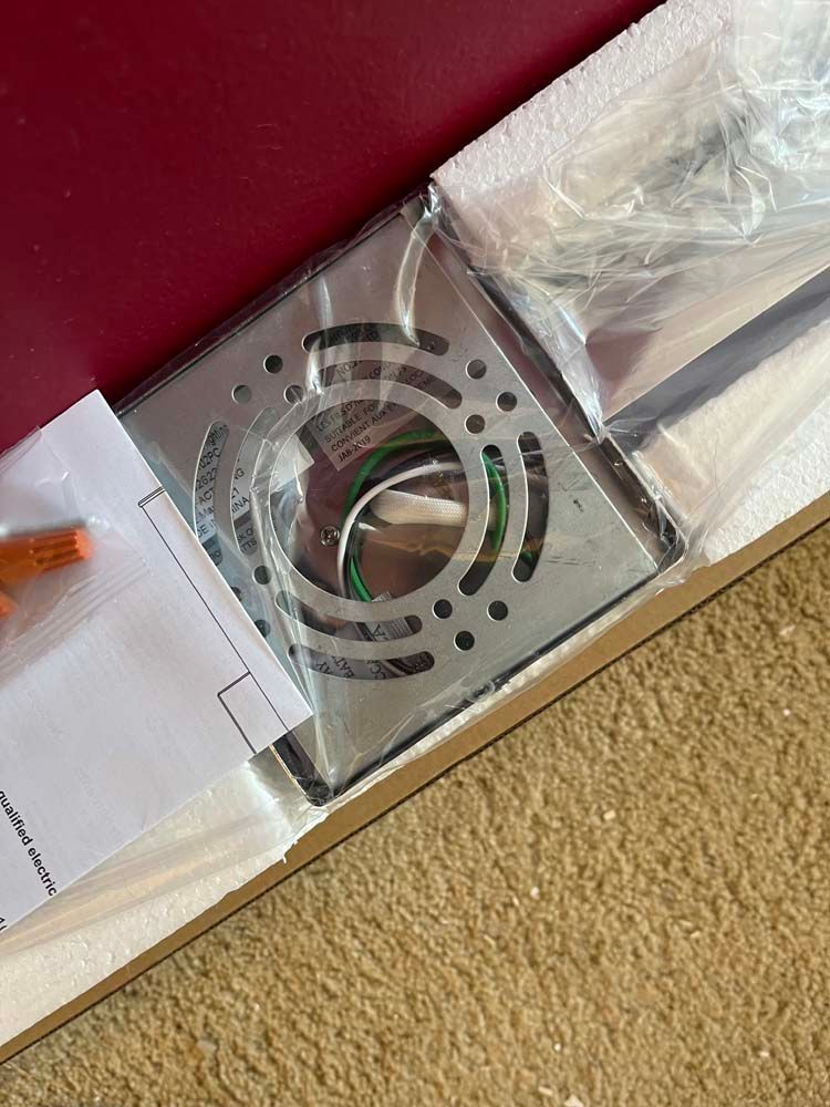 Metal vent grille and wrapped item in a box on a carpeted floor, next to a red surface