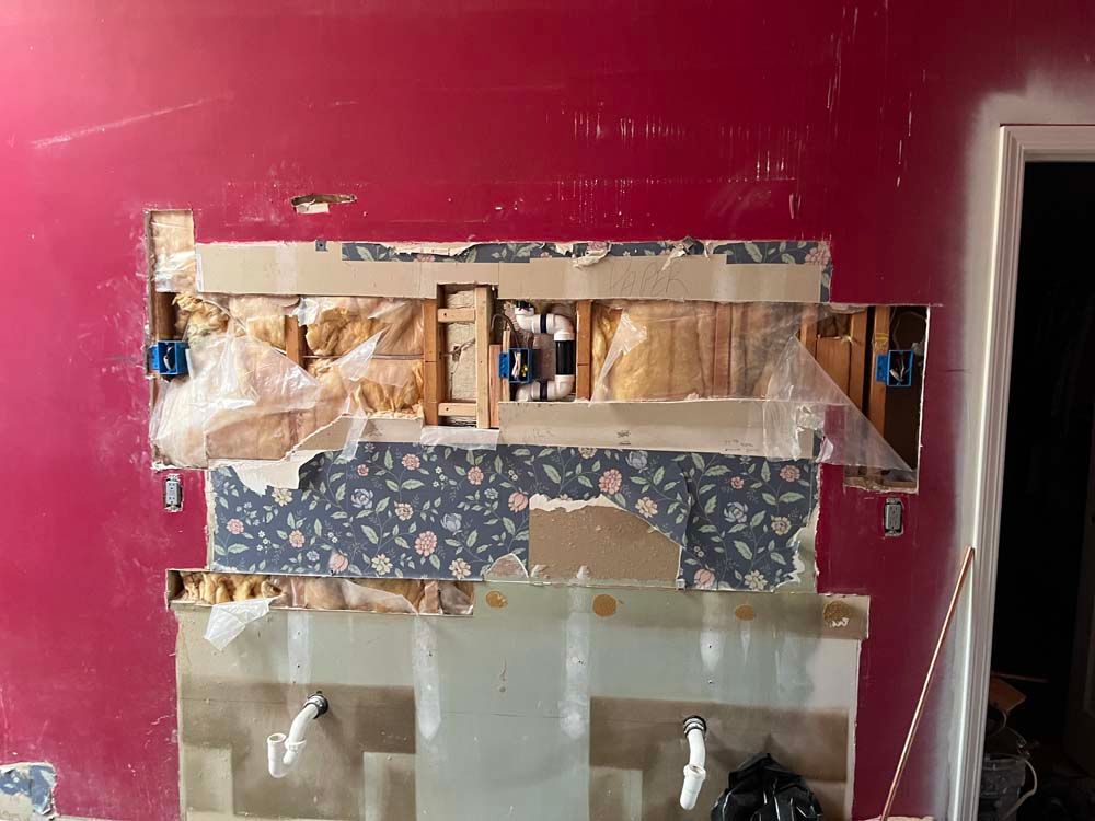 Damaged kitchen wall with exposed studs and drywall patches beneath a pink painted upper wall