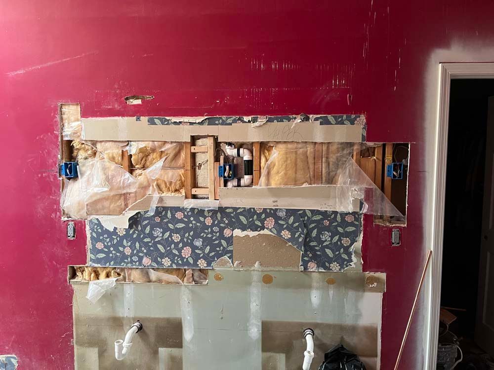 Partially stripped pink wall with exposed drywall and taped-over patches around a sink cutout