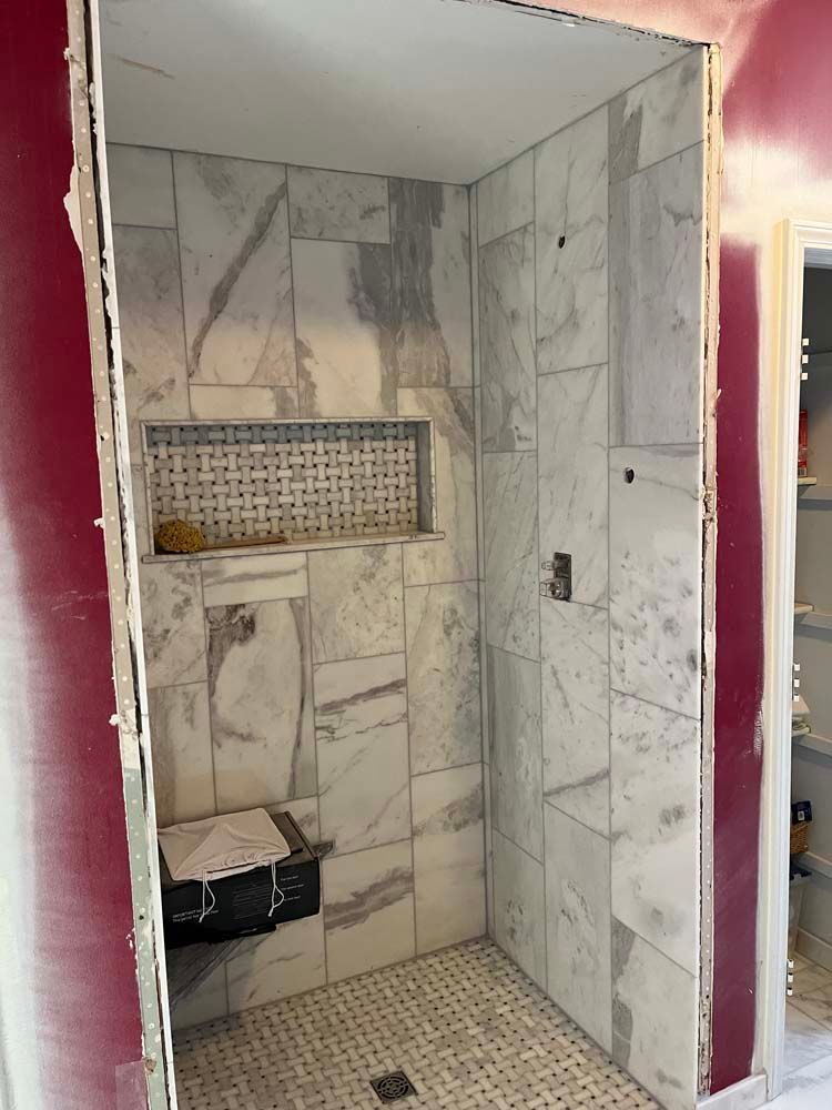 Marble-tiled shower stall with built-in shelves and mosaic floor, partially renovated in a bathroom.