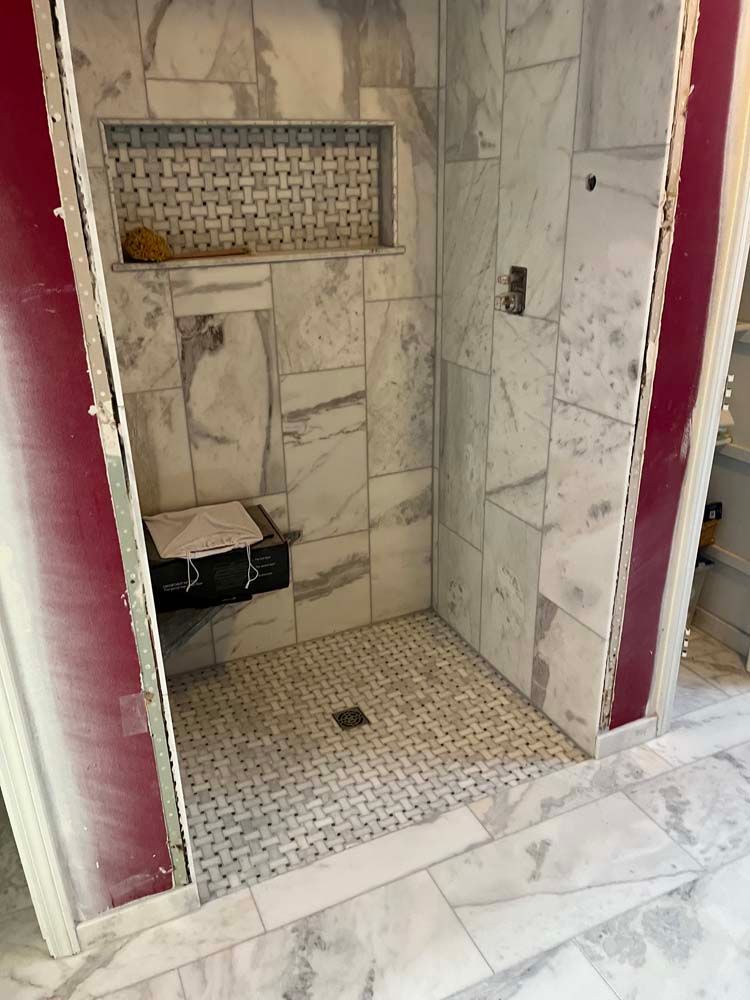 Marble-tiled shower stall with built-in shelf, drain, and open doorway.