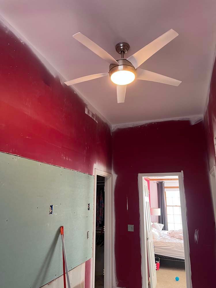 Narrow room with red walls, white ceiling fan, and open doorway to a brighter bedroom.
