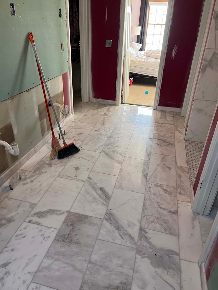 Marble-tiled hallway under renovation with a broom leaning by the wall and open doorway ahead