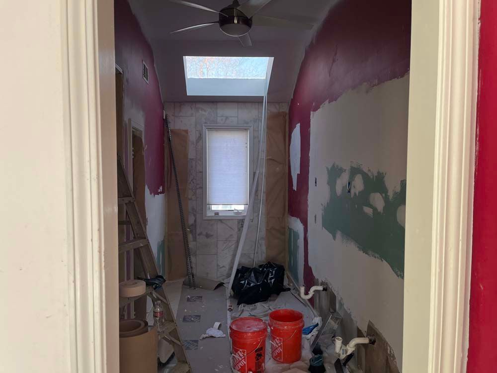 Narrow hallway under renovation with paint cans, tools, and a skylight at the far end