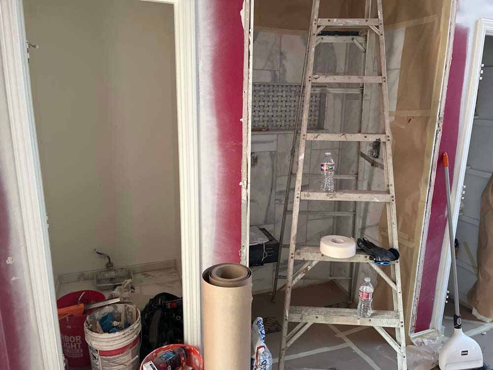 Construction area with ladder, paint buckets, and drywall in a partially renovated room