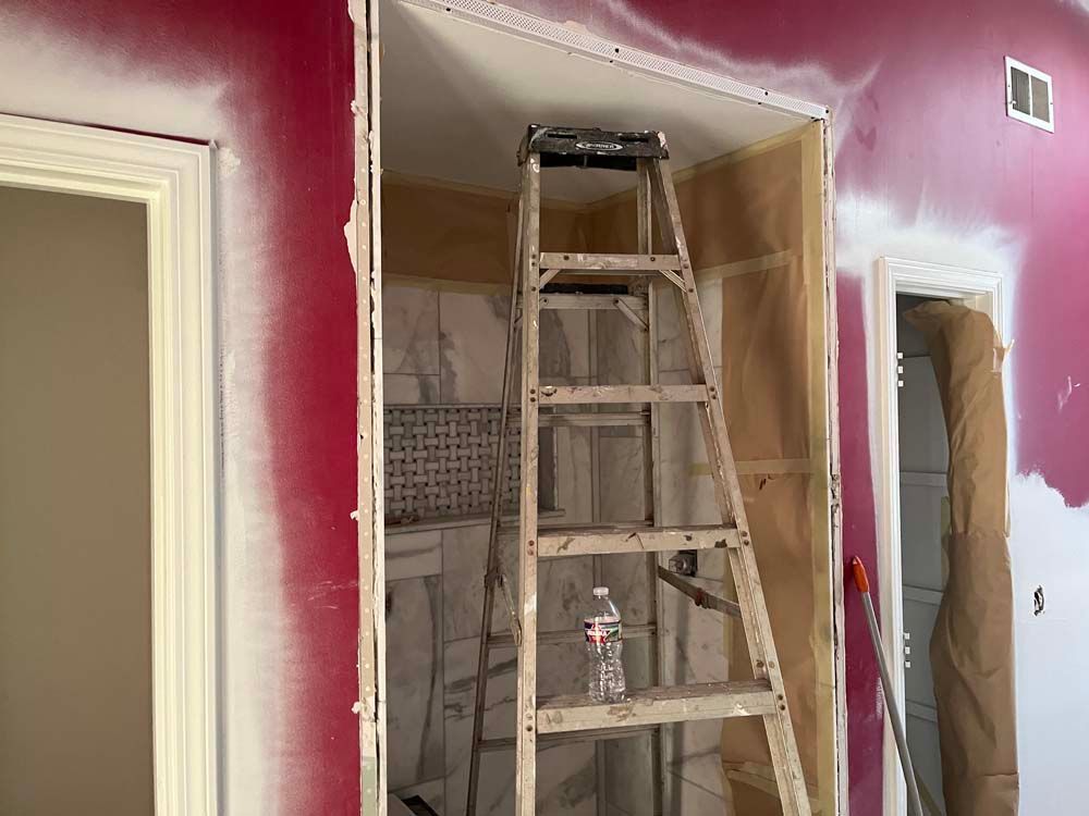 A ladder stands in a partially painted room with red walls and white trim, near an open closet.