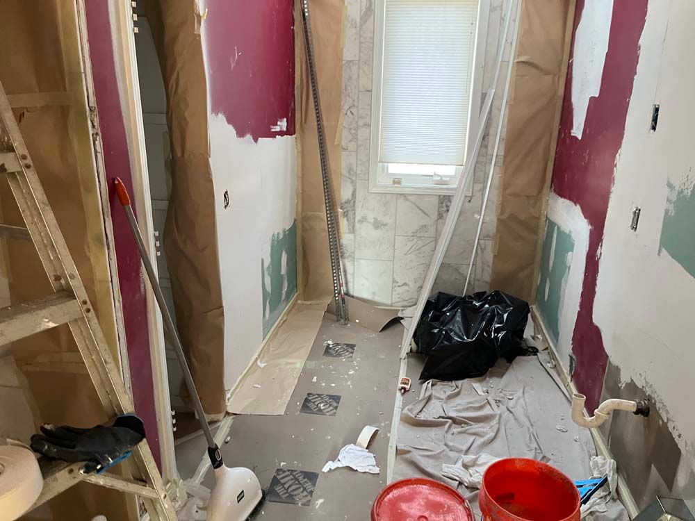 Narrow hallway under renovation with exposed drywall, tools, debris, a black trash bag, and a red bucket.