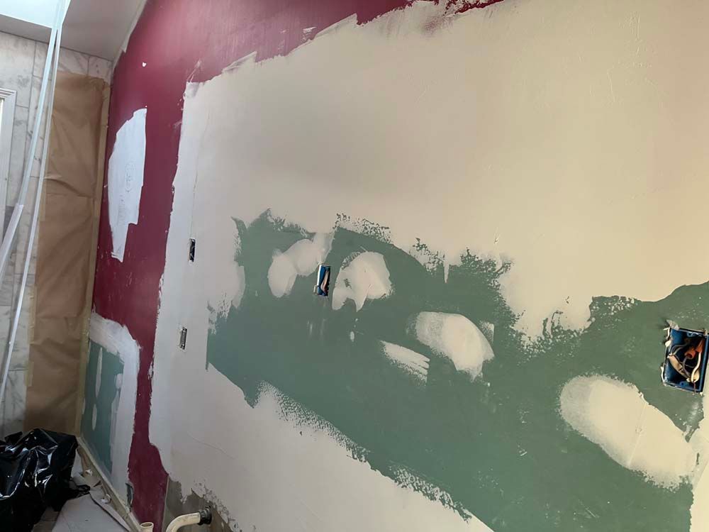 Partially painted drywall in a room, with green joint compound patches on a white wall and maroon edges