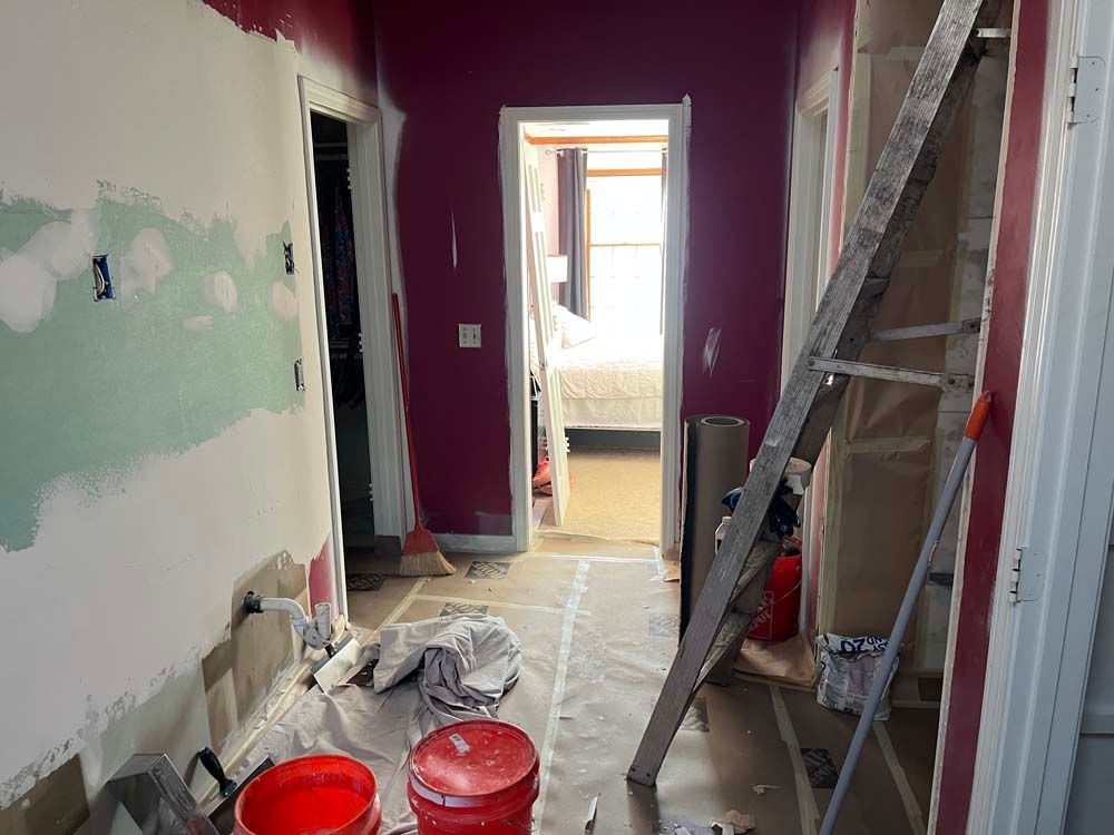 Partially renovated hallway with purple and green walls, ladder, buckets, and covered floor.