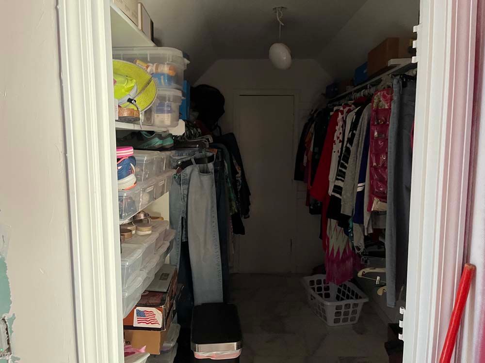 Narrow walk-in closet with clothes racks, shelves, storage bins, and a laundry basket