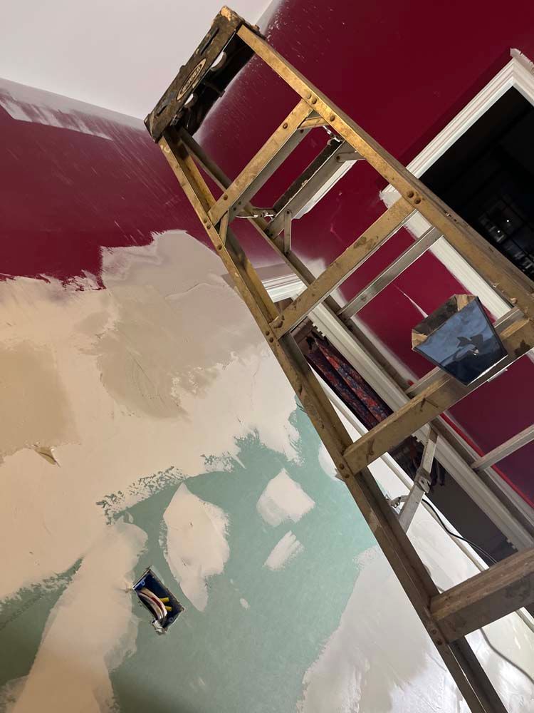 Partially painted wall and ceiling with exposed ladder in a room under renovation