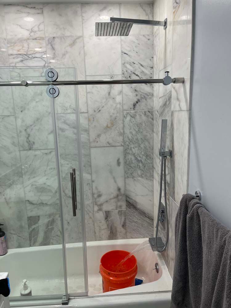 Glass shower with marble walls, rain showerhead, towel rack, and orange bucket in the tub.